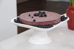 a chocolate cake with blueberries on top sits on a white plate next to a red vase