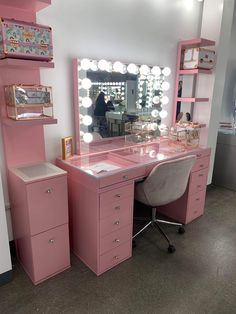 a pink vanity with lights on it and a chair in front of the mirror that is lit up