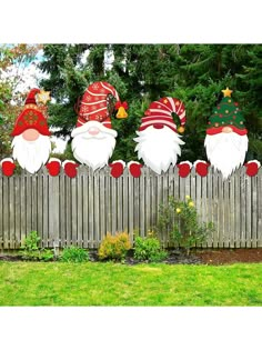 three christmas gnomes sitting on top of a wooden fence next to a green yard