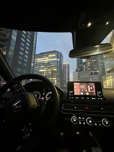 the interior of a car with city buildings in the background at night, showing dash lights and touchscreens