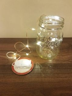 a mason jar with fairy lights and a small plate on a wooden table next to it