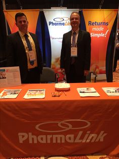 two men standing next to a table with pharmlink signs on it at an event