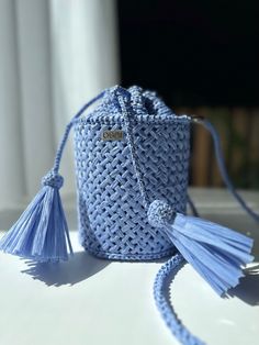 a small blue bag with tassels is sitting on a white table next to a window