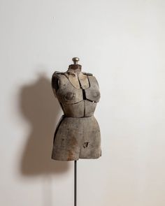 an old mannequin is standing on a metal stand in front of a white wall