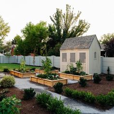 an outdoor garden with raised beds and wooden planters on the ground near a white fence