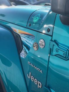 the side view of a blue jeep parked in a lot with other cars behind it