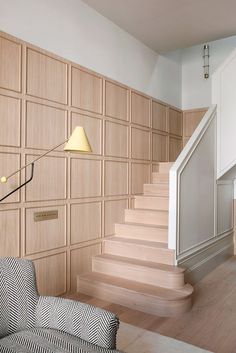 a living room filled with furniture and a stair case next to a wall mounted lamp