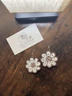 a pair of white flower earrings sitting on top of a wooden table next to a card