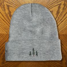 a grey beanie with trees on it sitting on top of a wooden table next to a