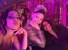 three women posing for the camera in front of purple lights