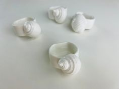 four white vases sitting next to each other on top of a table with shells around them