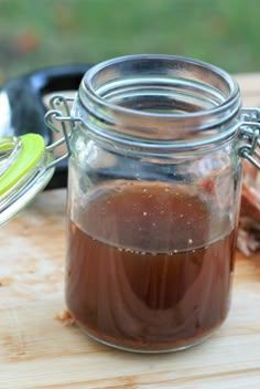 a jar filled with brown liquid sitting on top of a wooden table next to a spoon