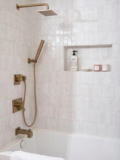 a white tiled bathroom with a shower head and hand held faucet in the bathtub