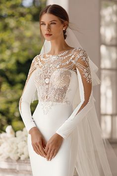 a woman in a white wedding dress with long sleeves and veil on her head is posing for the camera