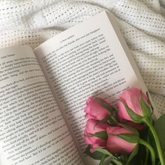 a pink rose sitting on top of an open book next to a white bed sheet