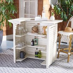 an outdoor bar with wine glasses, bottles and drinks on the shelves next to a potted plant