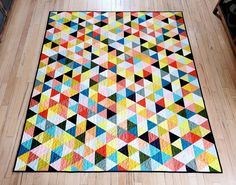 a multicolored quilt is laying on the floor in front of a wooden table