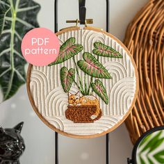 an embroidery pattern with a cat sleeping under a palm tree on a white background and text that reads pdf pattern