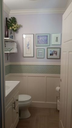 a white toilet sitting next to a bathroom sink under a light fixture with pictures on the wall above it