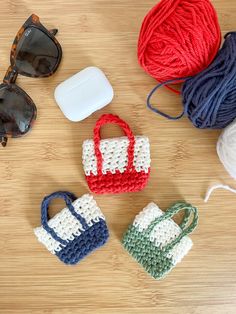 three crocheted purses and two balls of yarn on a wooden table with sunglasses