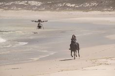 a person riding a horse on the beach with a remote control helicopter in the background