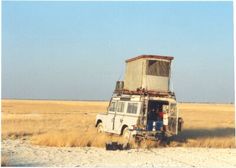 an old van is sitting in the middle of a field with its roof up and it's door open