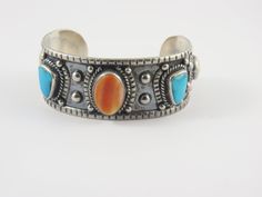 This is a sterling silver Native American  cuff bracelet with bezel set stones. An oval shaped orange colored Agate is set in the center with two irregular shaped Turquoise pieces on each side. There are white round stones set at each end. Each stone has  rope edging encircling the stones at  the base. The outer side of the bracelet has a darkened finish and there are silver ball accents across the top of the cuff. The inside of the bracelet has a dull silver finish. The cuff measures 5 1/2 " pl Oval Southwestern Sterling Silver Cuff Bracelet, Southwestern Silver Bracelet With Multi-stone, Southwestern Multi-stone Cuff Bangle Bracelet, Southwestern Multi-stone Cuff Bracelet, Southwestern Style Blue Nickel-free Cuff Bracelet, Stone Settings, Bezel Setting, Cuff Bracelet, Bangle Bracelets