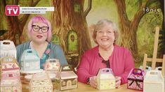 two women are sitting at a table with paper houses and boxes in front of them