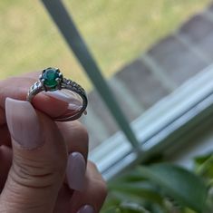 a woman's hand holding a ring with a green stone on it in front of a window