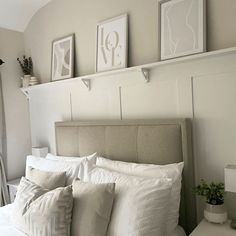 a bed with white linens and pillows in a small room next to pictures on the wall