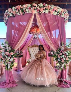 a woman in a pink wedding dress sitting on a chair under a canopy with flowers