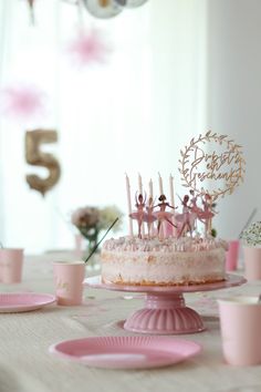 a birthday cake with pink frosting and little figurines sitting on top of it