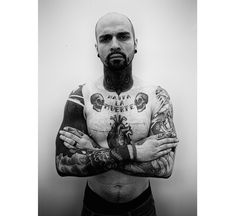 a man with tattoos on his arms and chest standing in front of a white wall