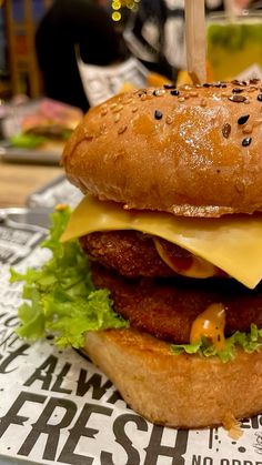 a cheeseburger with meat, lettuce and sauce on it sitting on a newspaper