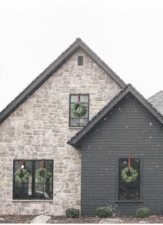 a gray house with wreaths on the windows and two christmas wreaths in the window