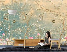 a woman sitting on the floor in front of a wall with flowers and birds painted on it