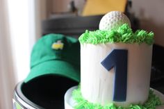 a birthday cake with a golf ball and green grass on the top, sitting on a table in front of a hat