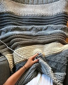 a woman is knitting a blanket on the couch