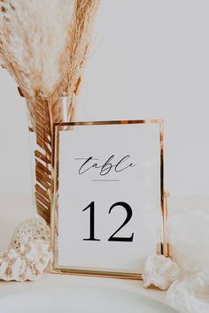 a table number is placed next to a vase with some dried flowers and feathers in it