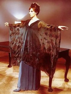 a woman in a blue dress is holding a black shawl over her shoulder and standing next to a piano