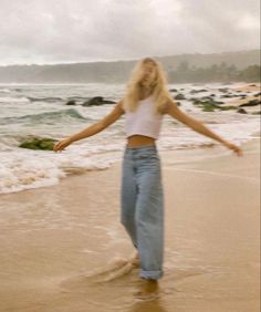 a woman is walking on the beach with her arms outstretched