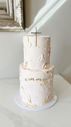 a white wedding cake with gold confetti and a cross on top is sitting on a table in front of a mirror