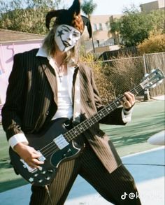 a man dressed as a clown playing an electric guitar in front of a fenced area