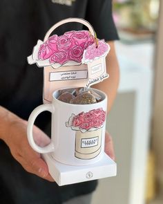 a person holding a coffee mug with pink roses on it and a tea bag in the middle