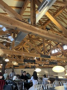 people sitting at tables in a restaurant with wood beams on the ceiling and exposed lighting