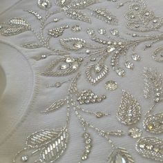 the fabric is white with silver beads and leaves on it's side, as well as an intricately embellished design