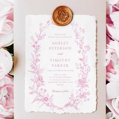 a pink and white wedding card with a wax stamp on it, surrounded by flowers