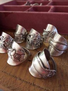 several silver rings sitting on top of a wooden table next to a red box with pink flowers