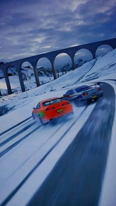 two cars driving down a snow covered road next to a bridge in the night time