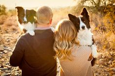 a man and woman are sitting with their dog on their shoulders in the desert at sunset